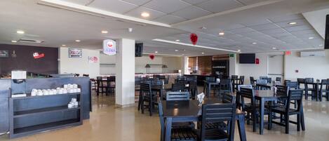 A spacious restaurant with multiple dining tables and chairs, a coffee station, and a kitchen area.