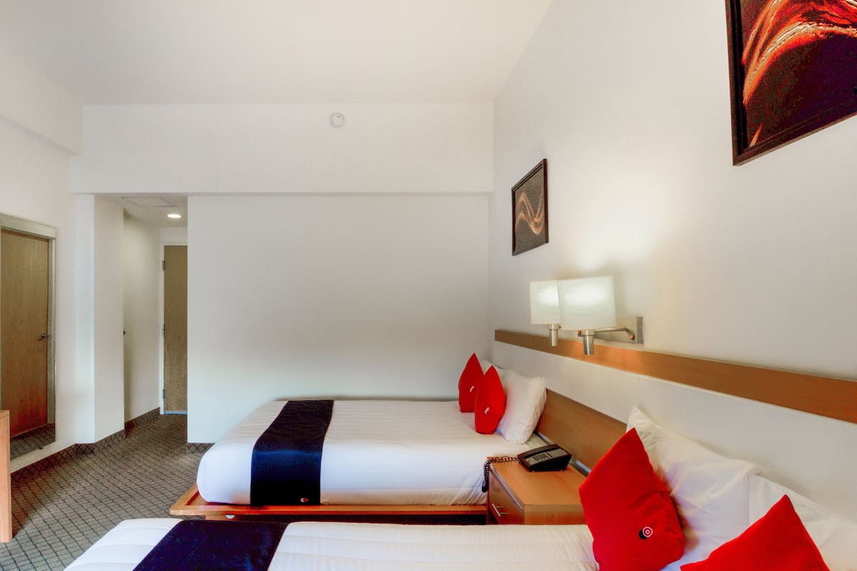 A hotel room with two beds, a bedside table with a lamp, a telephone, and a painting on the wall.