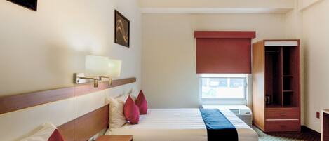 A hotel room with two beds, a bedside table with a lamp, a wardrobe, and a window with a view.