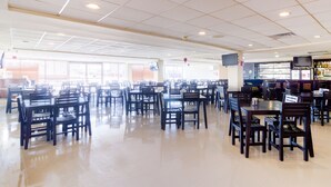 A spacious cafeteria with multiple tables and chairs, a bar area, and a television mounted on the wall.