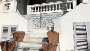 A staircase with white balustrades, a tiled wall with a tree and floral design, and terracotta planters with plants. - CasaVostra al Parco (Catania)