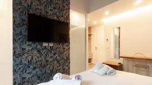 A hotel room with a bed, two rolled towels, a TV mounted on the wall, a mirror, and a wardrobe. - CasaVostra al Parco (Catania)