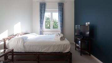 A bedroom with a bed, a TV, and a window with curtains.