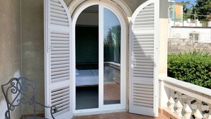 A balcony with a white balustrade, a metal chair, and a door with white shutters. - CasaVostra al Parco (Catania)