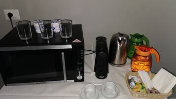 A kitchen area with a microwave, coffee maker, kettle, and a basket with snacks.