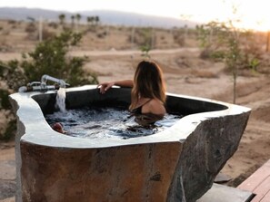 A woman sitting in a hot tub outdoors with a mountainous backdrop.
