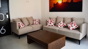 A living room with two sofas, a coffee table, and a painting of a sunset skyline. - Hotel Dwana (Mazatlán)