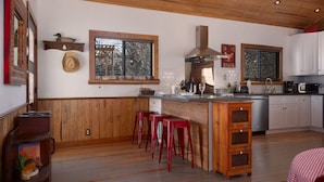 Une cuisine avec des meubles de rangement en bois, un îlot central doté de tabourets, une grande fenêtre et un chapeau suspendu.