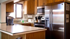 A kitchen with wooden cabinets, stainless steel appliances, a microwave, a refrigerator, a sink, and a window.