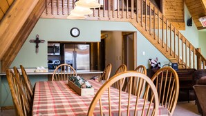 A dining area with a wooden table and chairs, a kitchen with appliances, and a staircase leading to an upper level.