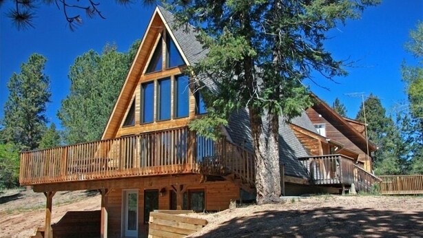 A wooden cabin with a large deck, a covered porch, and a steeply pitched roof.