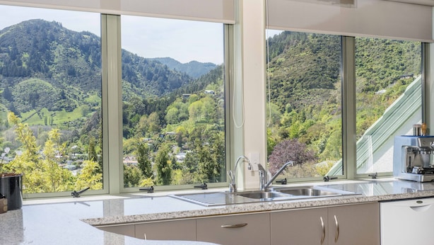 A kitchen with large windows offering a view of a green valley and hills. - Hilltop Getaway - Superb Sea & Mountain Views with Spa pool! (Nelson)