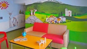 A room with a striped sofa, a small table with a globe and books, a red chair, and a mural of a village scene. - Surses Alpin by Interhome (Savognin)