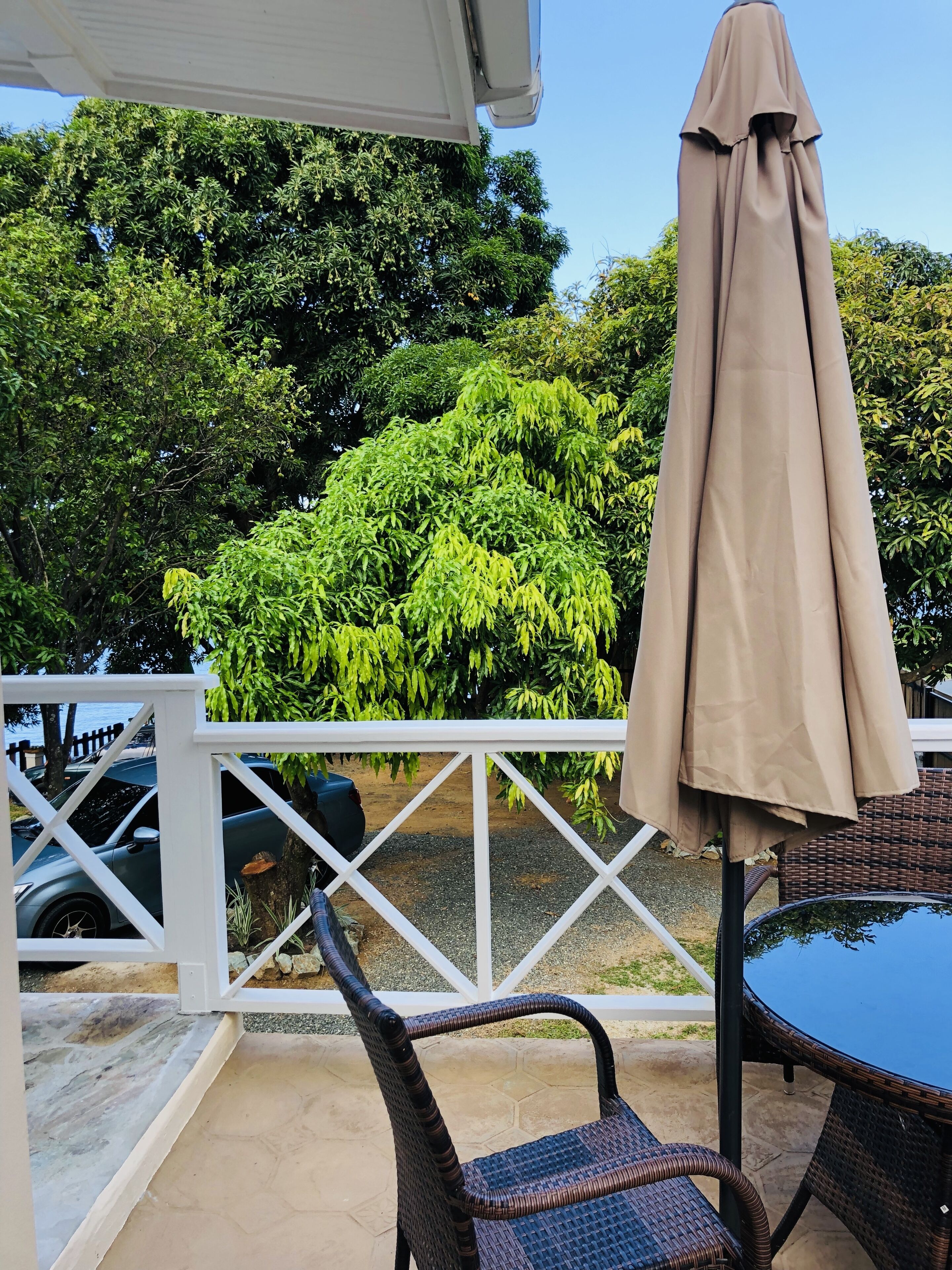 Un espace patio extérieur doté d’une balustrade blanche, d’une table, de deux chaises en osier et d’un parasol beige.