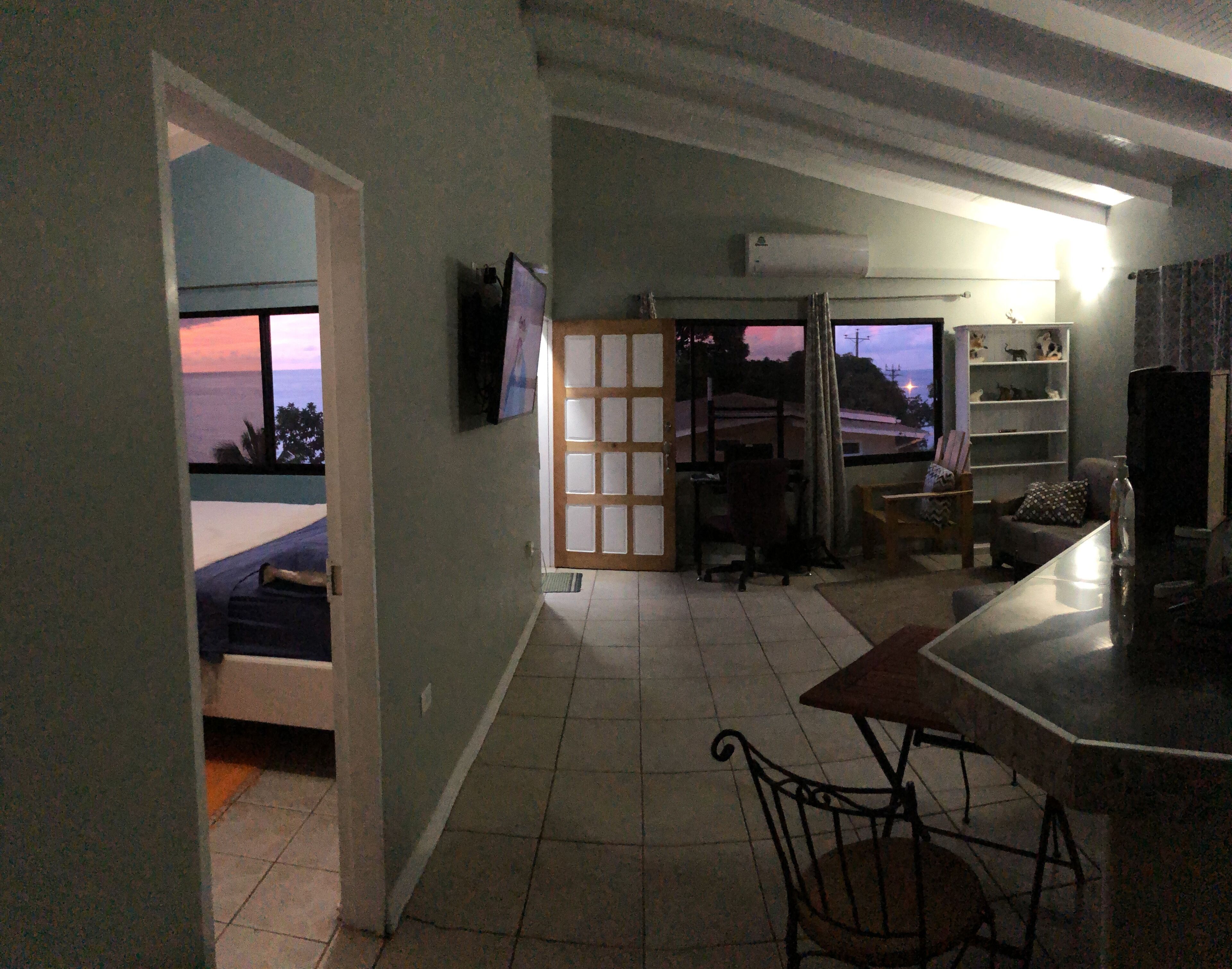 Ein Wohnzimmer mit Blick auf den Sonnenuntergang, einem an der Wand befestigten Fernseher und einer Bar mit einem Stuhl.