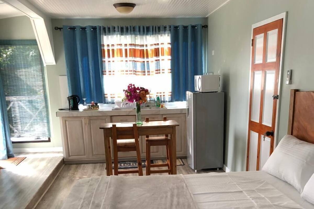 Une chambre à coucher avec un lit, un bureau et une chaise, un réfrigérateur et une fenêtre avec des rideaux.