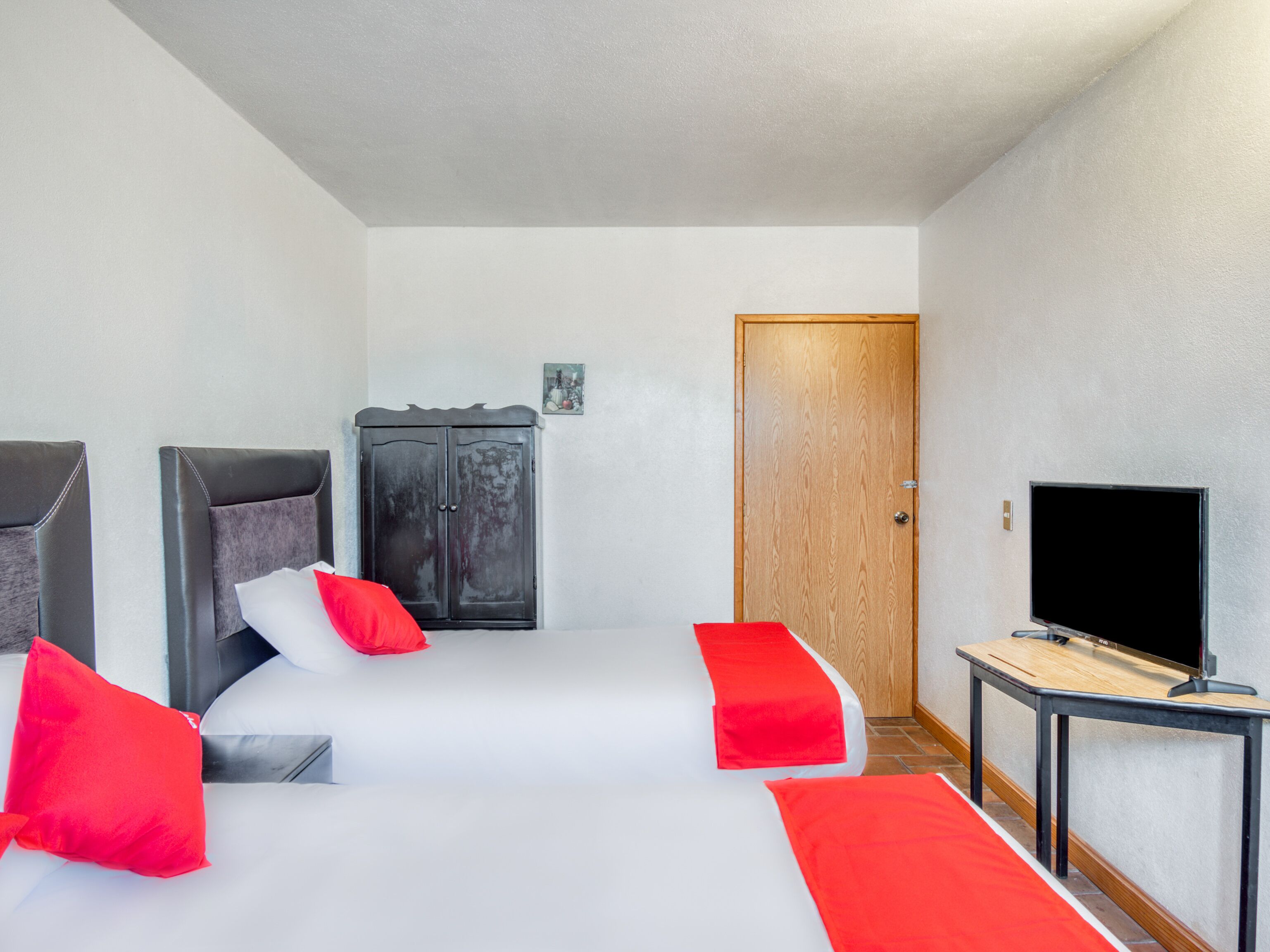 A hotel room with two beds, a wardrobe, a television, and a door.