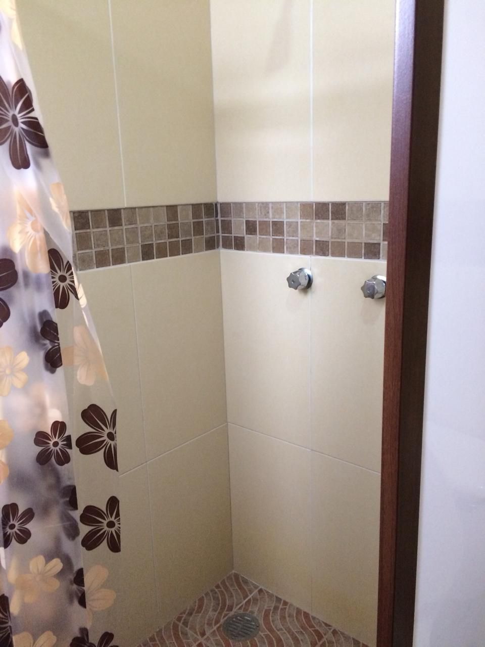 Un espacio de ducha pequeño con azulejos y una cortina decorada con un estampado floral.