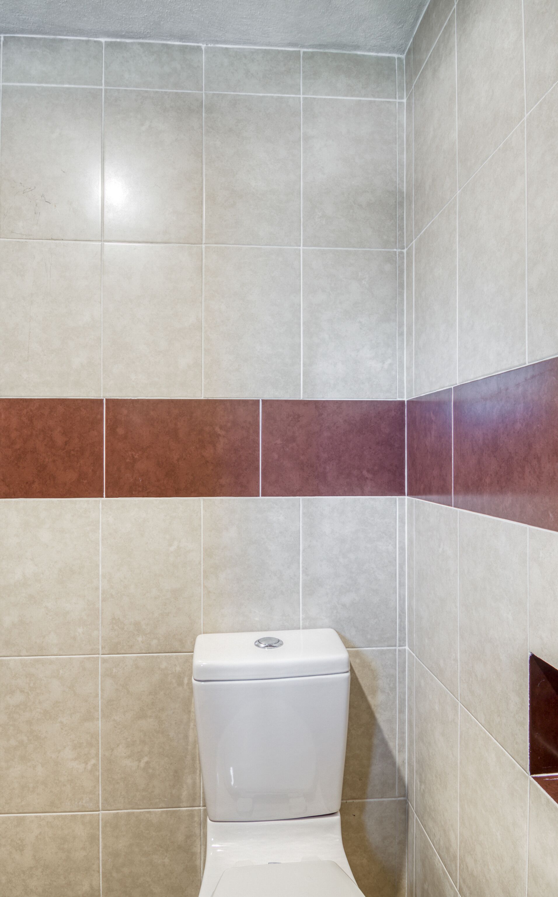 A bathroom with a toilet, tiled walls, and a brown accent strip.