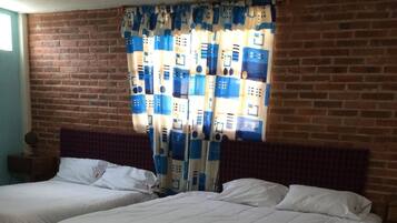 Una habitación con dos camas, una pared de ladrillo y una cortina de estampado geométrico.