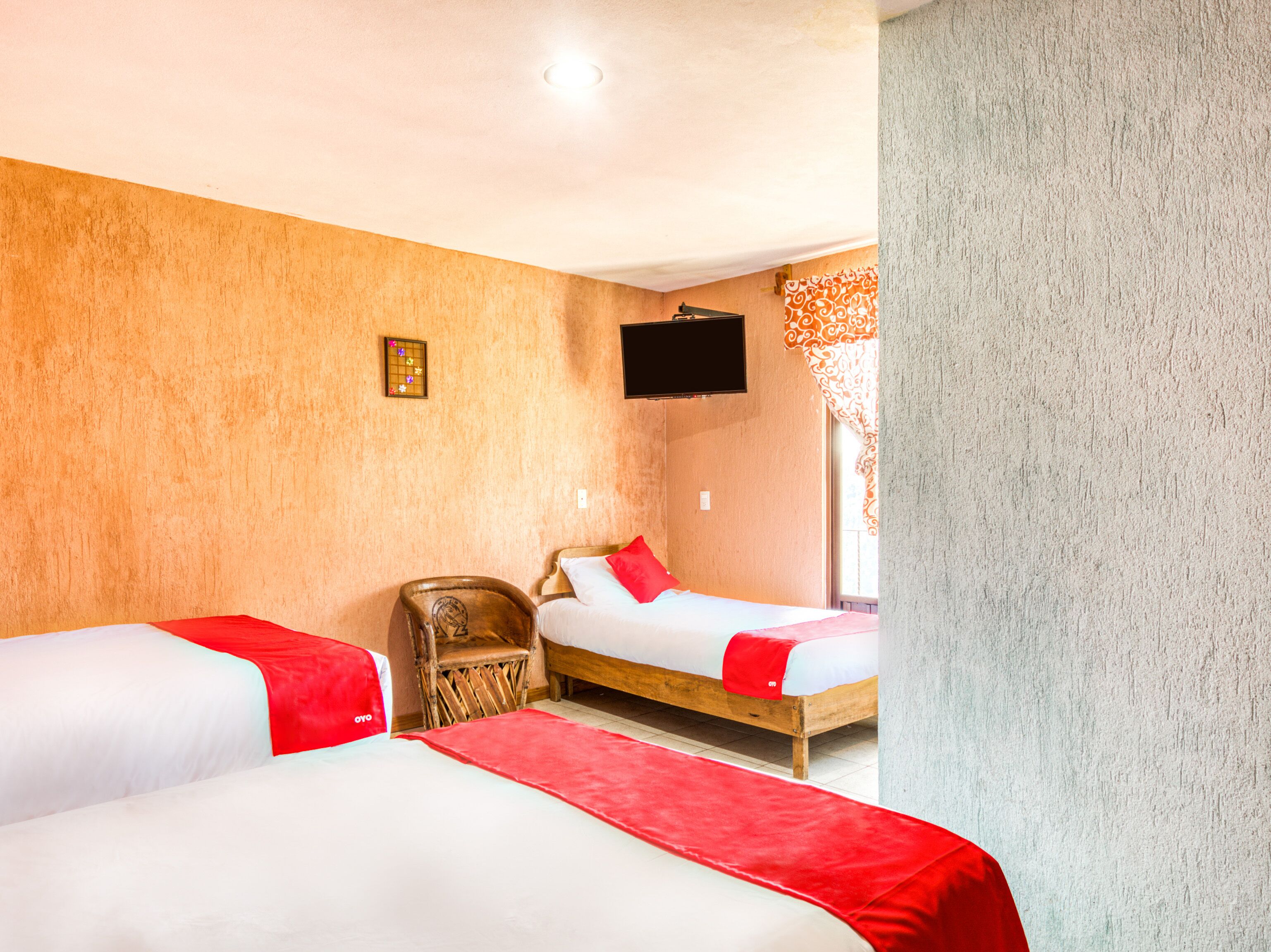 A hotel room with two beds, a wooden chair, a television, and a patterned curtain.