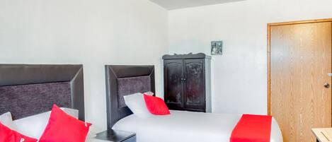 A hotel room with two beds, each with white bedding and red pillows, a dark wooden wardrobe, and a wooden door.