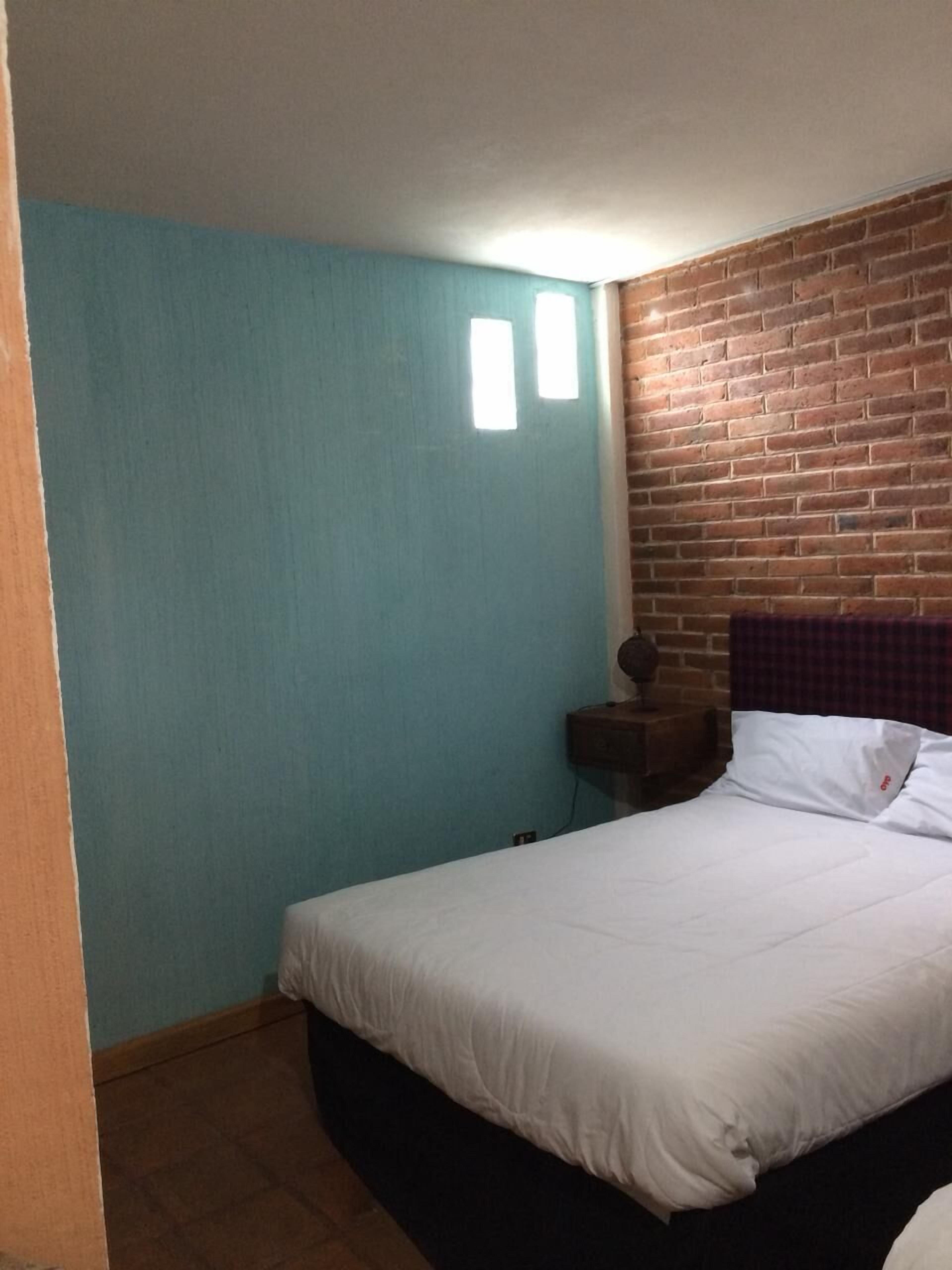 Un dormitorio con una cama individual, pared de ladrillo y una pared color turquesa.
