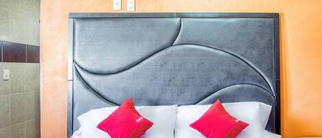 A hotel room with a grey upholstered headboard, white bedding, and two red pillows.