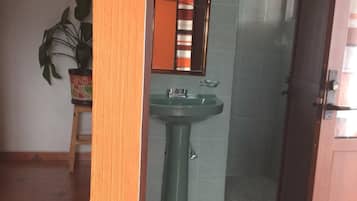 Un baño con lavamanos verde, un espejo y una zona de ducha.