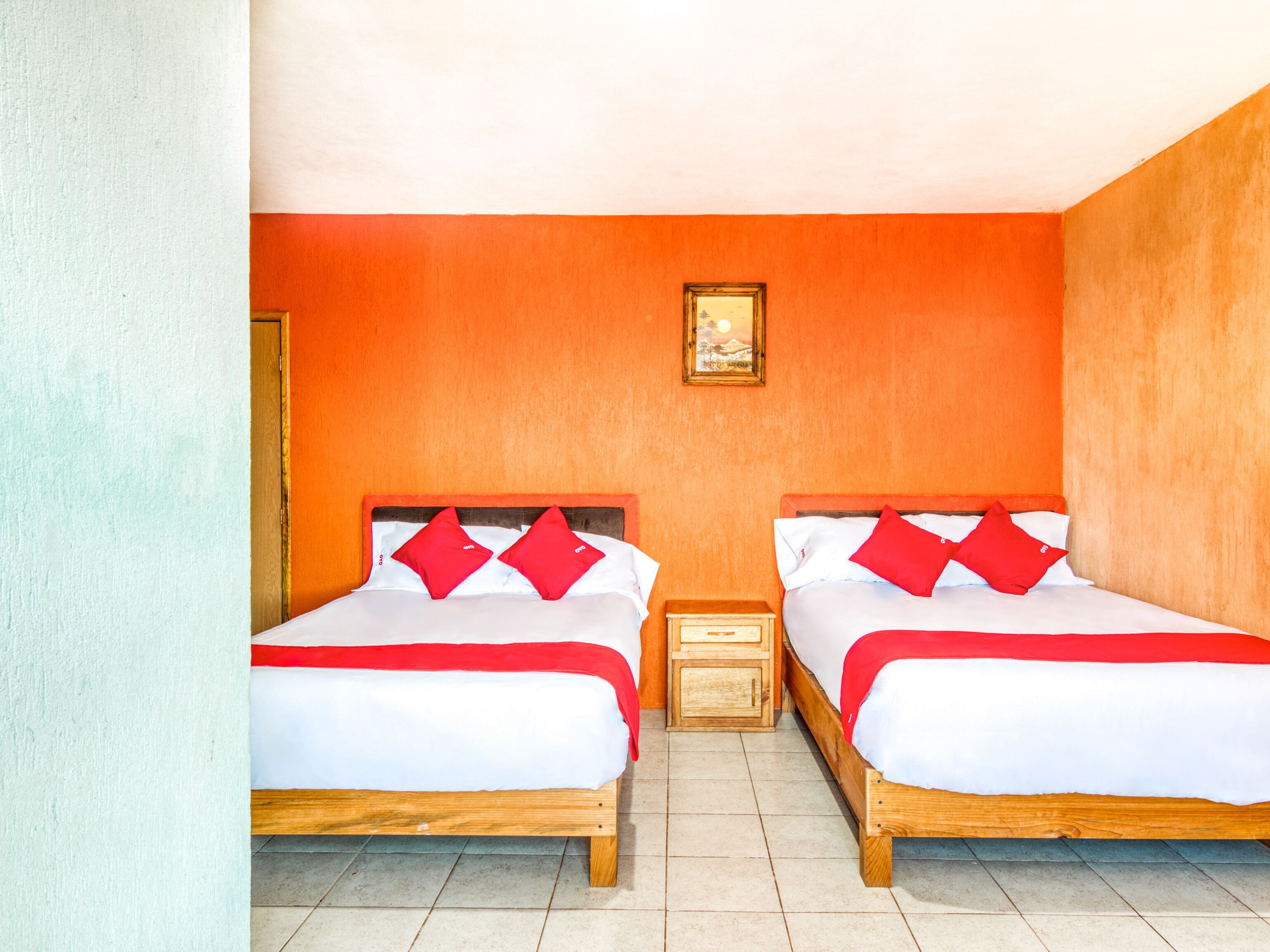 Habitación de hotel con dos camas, cada una con almohadas rojas y ropa de cama blanca, cabeceros de madera y una mesita de noche de madera entre ellas.