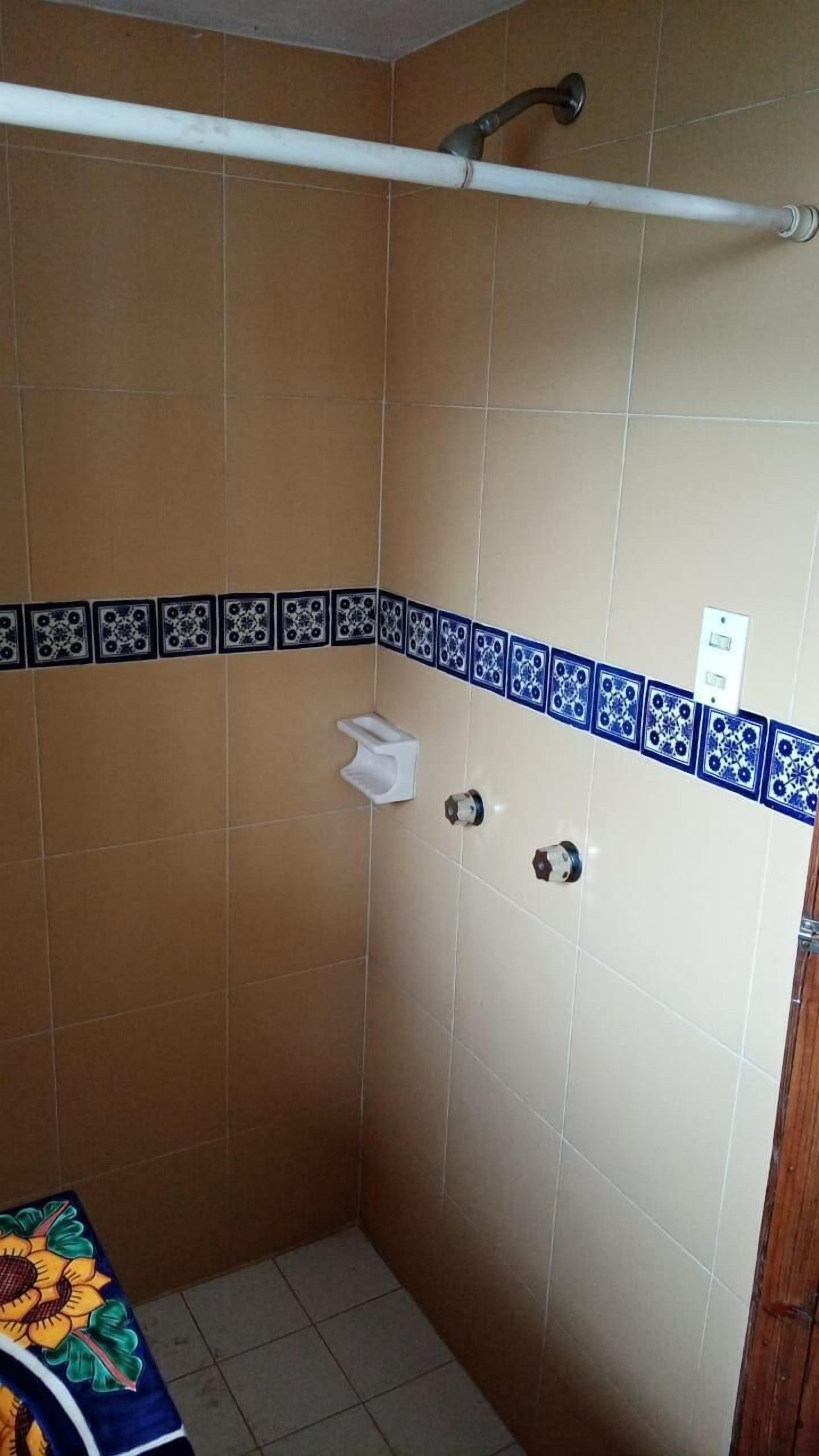 A small bathroom with beige tiles, a shower area, a towel rack, and a toilet.