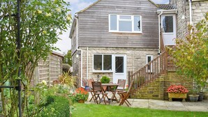 A two-story house with a stone facade, a wooden staircase, and a small garden with a table and chairs. - 2 bedroom accommodation in Chideock (Chideock)
