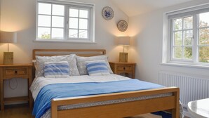 A bedroom with a wooden bed, two bedside tables, a nightstand, a window, and a wall-mounted lamp. - 2 bedroom accommodation in Chideock (Chideock)