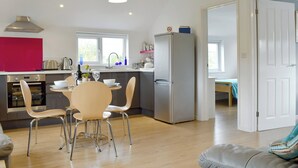 A modern kitchen with a dining area, wooden beams, a clock, and a refrigerator. - 2 bedroom accommodation in Chideock (Chideock)