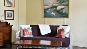 Um quarto com um sofá roxo, uma mesa de madeira e um quadro de cisnes na parede.
