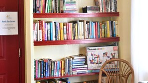 Uma estante com livros e objetos decorativos, uma cadeira de vime e uma porta vermelha.