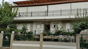 Ein zweistöckiges Gebäude mit Balkon, geschlossenem Eingangsbereich und einem kleinen Garten.