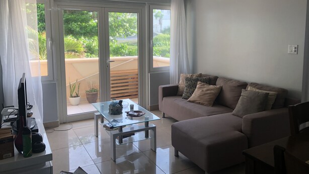 Un soggiorno con tavolino in vetro, divano color beige e ventilatore a soffitto.