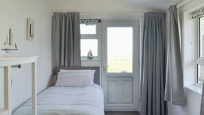 Quarto com cama, escrivaninha, janela com cortinas e vista para o exterior.