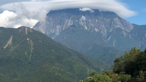 A mountain with a cloud formation on top, surrounded by lush green hills.