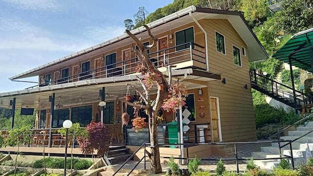A two-story building with a balcony, surrounded by greenery and stairs leading up to it.
