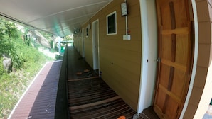 A covered corridor with wooden doors, a small window, and a power outlet on the wall.