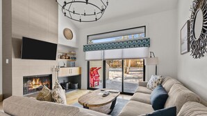 A modern living room with a fireplace, a large sofa, a coffee table, and a view of a snowy outdoor area. - RMR: Cinquefoil 1615 Condo in The Aspens/Wilson,WY (Wilson)