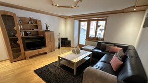 Een moderne woonkamer met een zwarte leren bank, een houten entertainmentmeubel en een zwart pluisachtig vloerkleed.