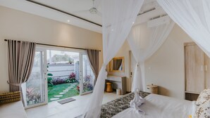A bedroom with a bed, a bedside table, a wardrobe, and a view of a garden through a sliding door. - Rommy Villas Lembongan (Lembongan Island)