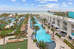 Um resort com várias piscinas, palmeiras e vista para o oceano.