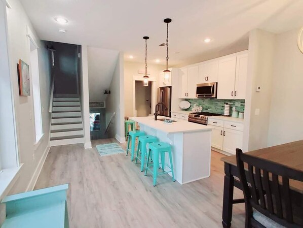 A modern kitchen with white cabinets, a central island with bar stools, and a dining area with a wooden table and chairs.