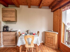 Une petite cuisine avec une table dressée pour deux personnes, des placards en bois et une fenêtre avec un rideau.