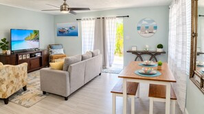 A living room with a sofa, a television, a dining table with placemats, and a ceiling fan.