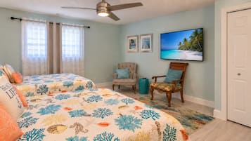 Un dormitorio con dos camas, ventilador de techo, televisor y una puerta.